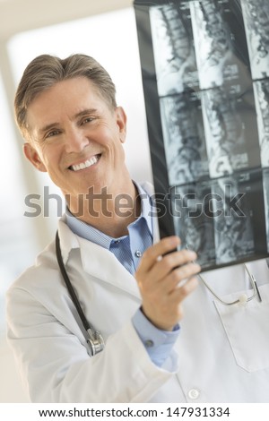 Portrait of happy male doctor holding X-ray image while standing in clinic