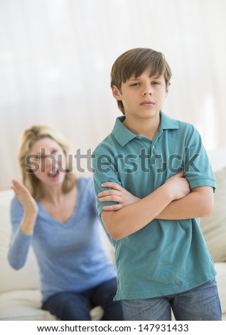 Son standing arms crossed while ignoring angry mother at home