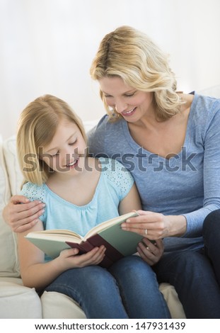 Happy mother and daughter reading book together on sofa at home