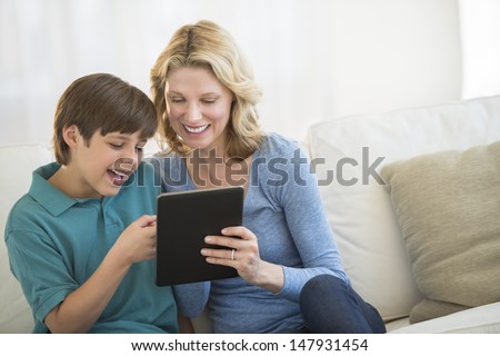 Happy mature woman and son using digital tablet together on sofa at home