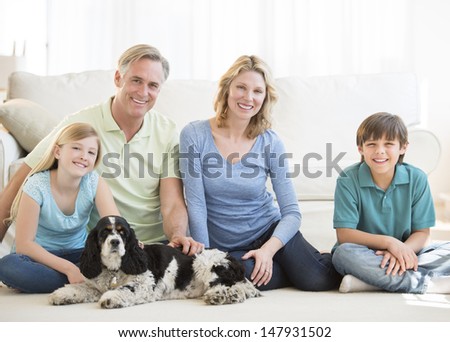 Portrait of happy family of four with pet dog sitting on floor in living room at home