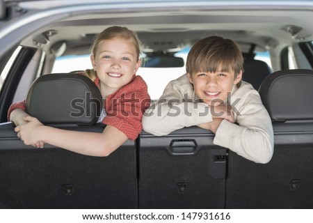Portrait of happy brother and sister leaning on car seat