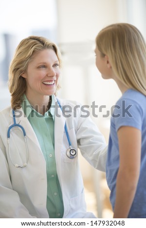 Happy female doctor with stethoscope around neck looking at girl in hospital