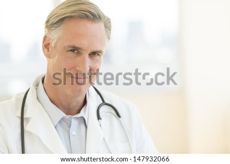 Portrait of confident mature male doctor with stethoscope around neck in clinic