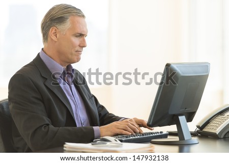 Serious mature businessman using desktop PC in office
