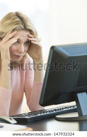 Frustrated mature businesswoman with head in hands looking at computer