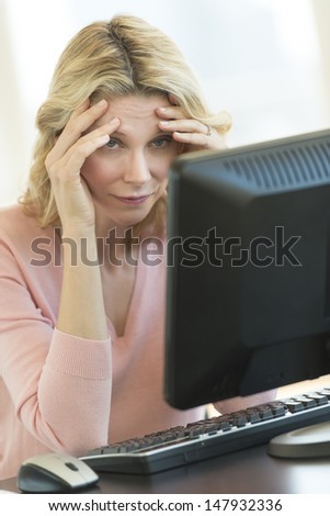 Depressed mature businesswoman with head in hands looking at computer monitor