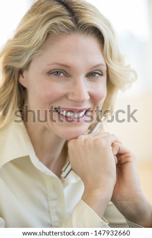 Close-up portrait of happy businesswoman with hand on chin in office