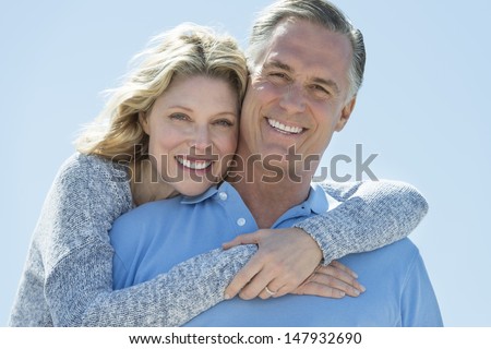 Portrait Of Loving Mature Woman Embracing Man From Behind Against Clear Blue Sky