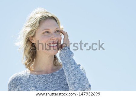 Beautiful mature woman with hand in hair looking away against clear sky