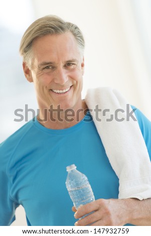 Portrait of happy mature man with water bottle and towel at gym