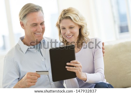 Happy mature couple with credit card and digital tablet shopping online at home