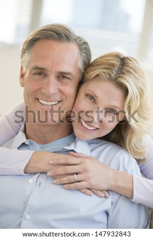 Portrait of happy mature woman embracing man from behind at home
