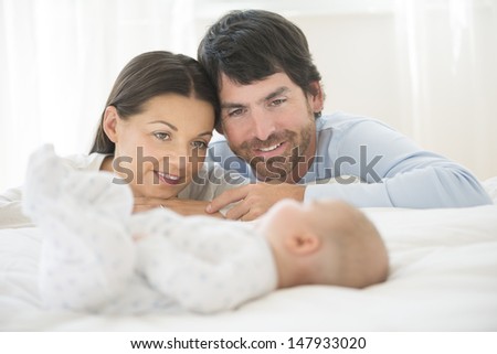 Smiling young couple looking at a blurred little baby sleep in bed at home