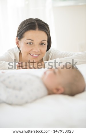 Smiling young woman looking at a blurred little baby sleep in bed at home