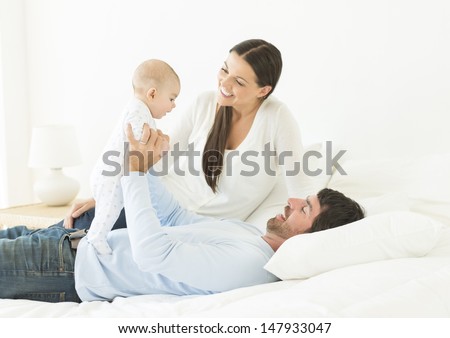 Happy young parents playing with little baby in bed