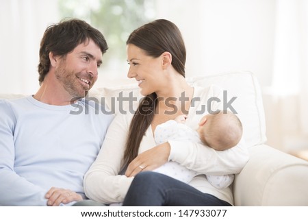Relaxed young couple with cute little baby sitting on couch