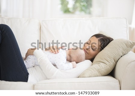 Side view of a young woman with baby sleeping on couch at home