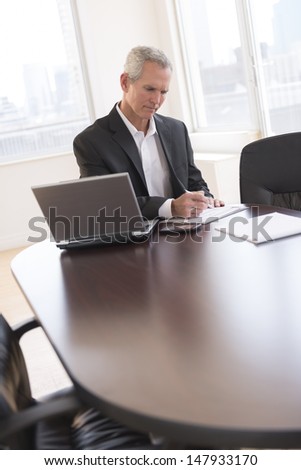Mature businessman writing on document at desk in office