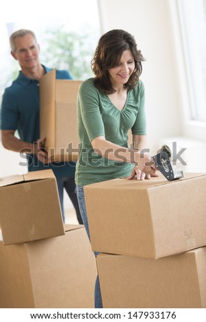 Mature woman packing cardboard box with man standing in background at home