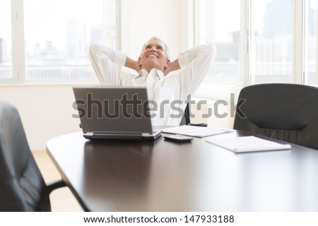 Relaxed mature businessman with hands behind head sitting at desk in office