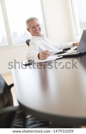Portrait of mature businessman smiling while writing on document at desk in office