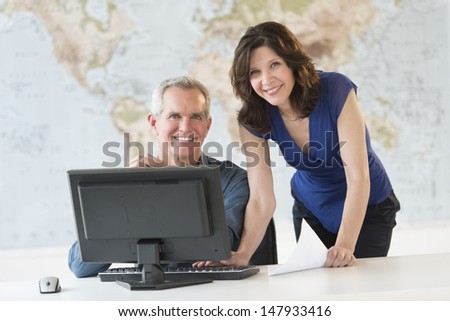 Portrait of happy business people working at office desk with world map in background