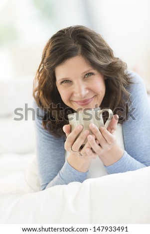 Portrait of beautiful mature woman holding coffee mug while relaxing in bed at home