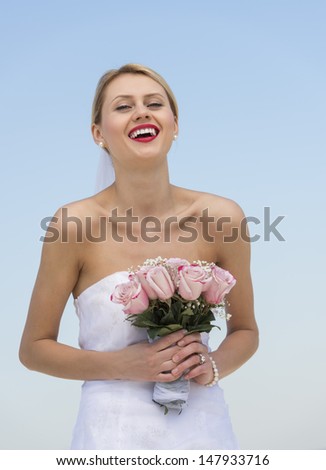 Portrait of happy young bride holding flower bouquet against clear blue sky