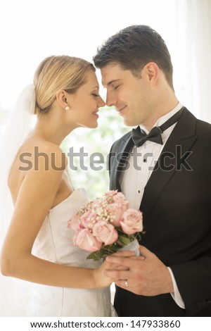 Newlywed young bride and groom with flower bouquet rubbing noses