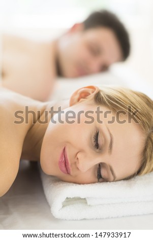 Closeup of beautiful young woman resting on massage table with man in background at spa