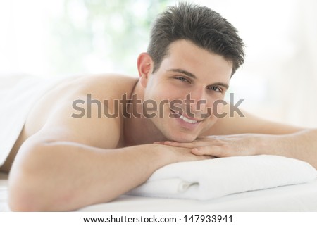 Portrait of young man resting on massage table at health spa