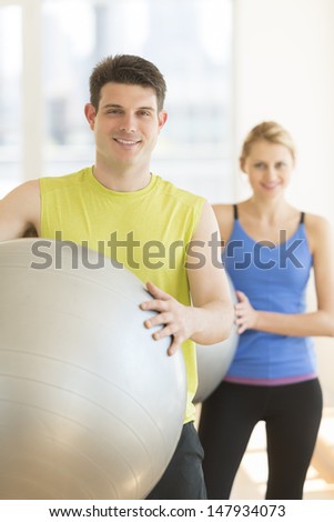 Portrait of confident young couple with fitness balls in gym