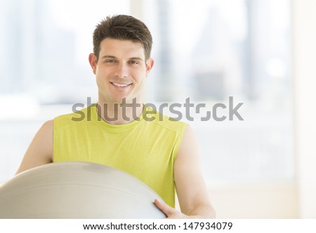 Portrait of young man with fitness ball smiling in gym