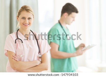 Portrait of beautiful female doctor standing arms crossed with male colleague in background at hospital