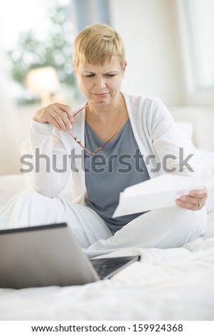 Woman reading letter while sitting on bed