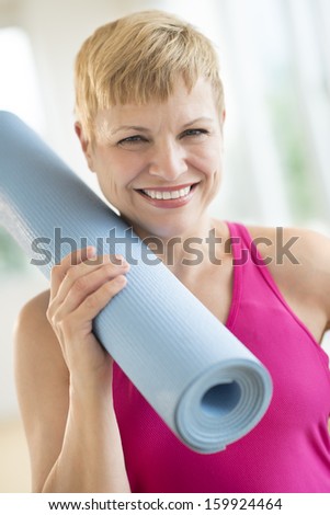 Woman holding rolled up exercise mat at gym
