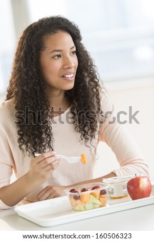 Teenage student eating fruit salad in university canteen