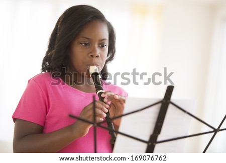 Little girl looking at sheet music while playing flute at home