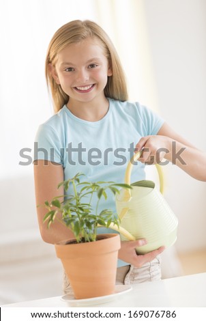 Portrait of happy girl watering potted plant at home