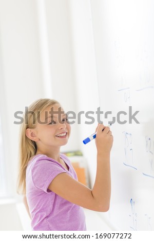 Portrait of happy girl with felt tip pen solving math problem on whiteboard in classroom