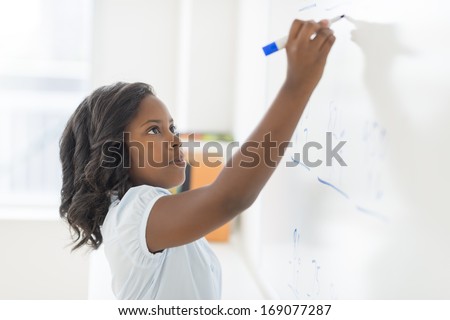 Side view of African American girl solving math problem on whiteboard in classroom