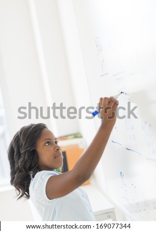Side view of schoolgirl solving math problem on whiteboard in classroom