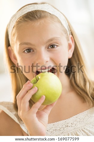 Closeup portrait of cute girl eating granny smith apple at home