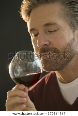 Handsome mature man smelling red wine isolated on black background