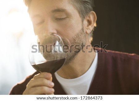 Mature man smelling glass of red wine at home