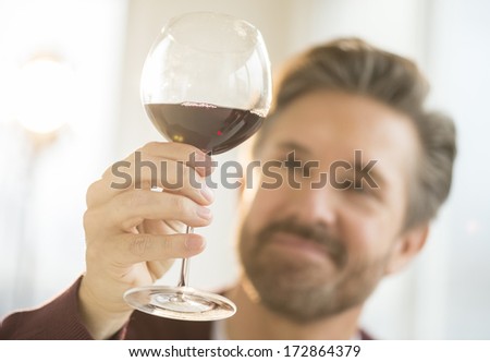 Mature man holding glass of red wine at home