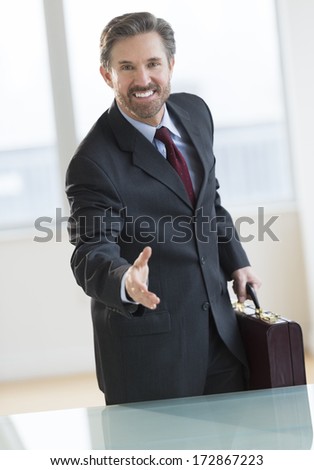 Portrait of mature businessman offering hand at desk in office
