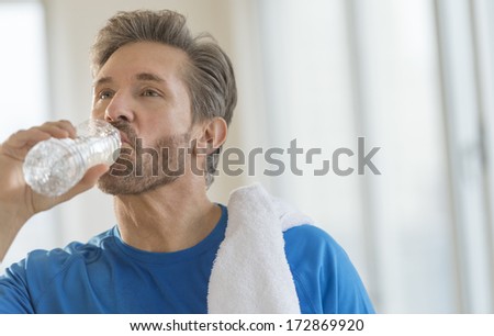 Mature man drinking water from bottle after exercising at home
