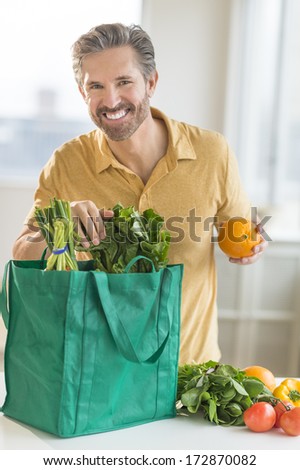 Portrait of happy mature man unpacking bag of groceries at counter top